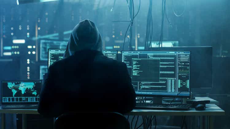 Gevaarlijke Hooded Hacker breaks into regering data servers in a human system with a virus infected.  Zijn schuilplaats plek heeft donkere sfeer, meerdere beeldschermen, cables overal.